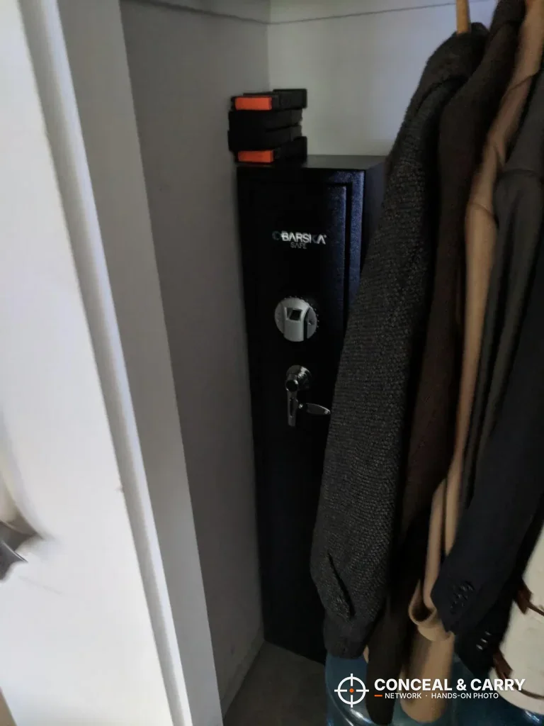 Barska biometric rifle safe standing in a closet beside hanging coats