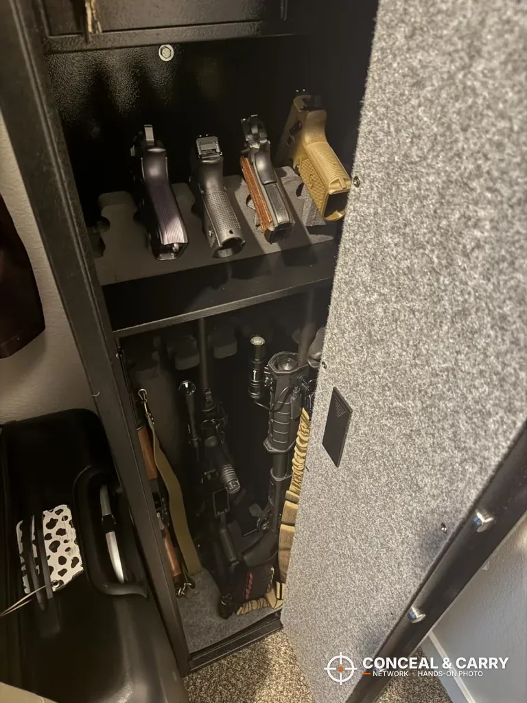 Handguns standing in a rack on the BBRKIN rifle safe shelf with long guns below