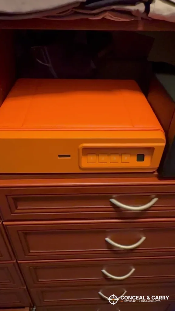 Orange BBRKIN Slide-Away safe sitting on a wooden chest of drawers
