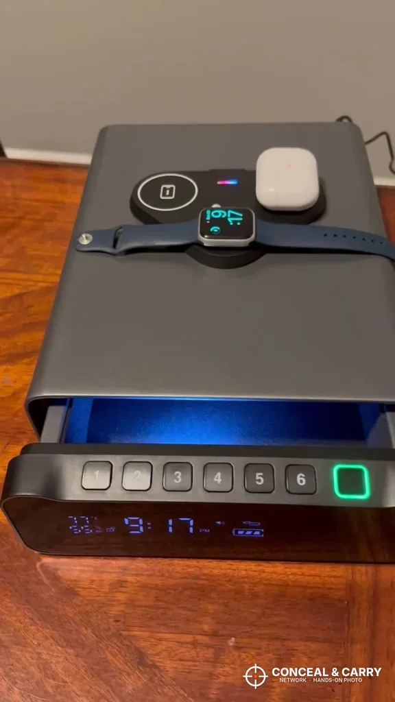 FTOP clock gun safe on a nightstand with a watch and earbuds on the charging pad and the drawer open
