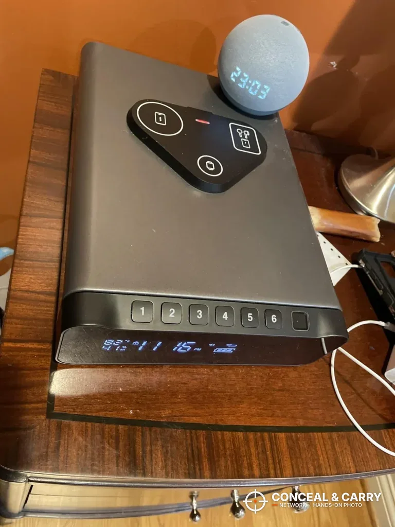 FTOP clock gun safe on a nightstand with the keypad and clock lit and a smart speaker on top
