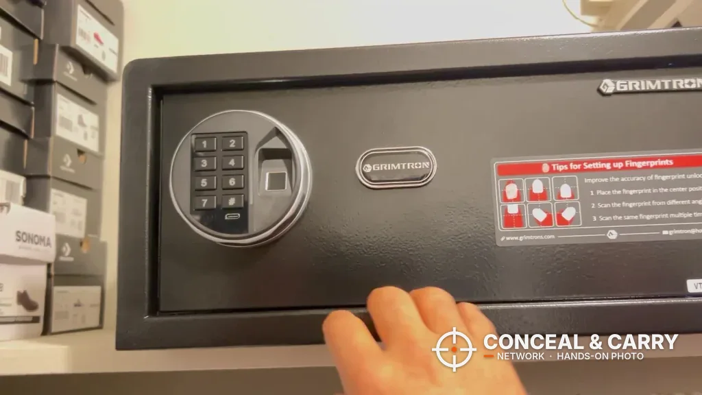 Hand at the bottom edge of the Grimtron 4-pistol safe front to show its size