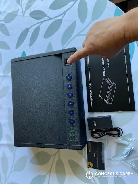 Grimtron heavy-duty biometric safe laid out with its manual and cables, a finger pointing at the reader