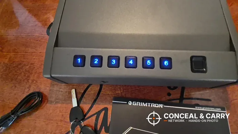 Grimtron heavy-duty biometric safe with its six keypad buttons lit blue, keys and cable beside it