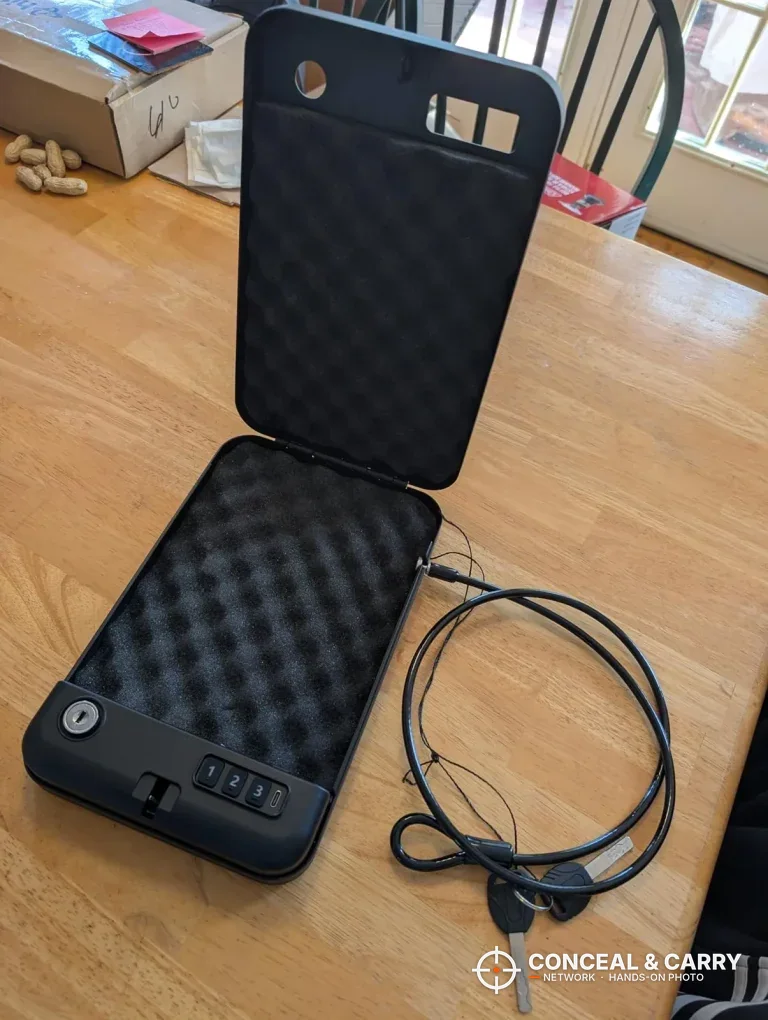 Grimtron portable car gun safe open with foam lining in the lid and base and the security cable beside it
