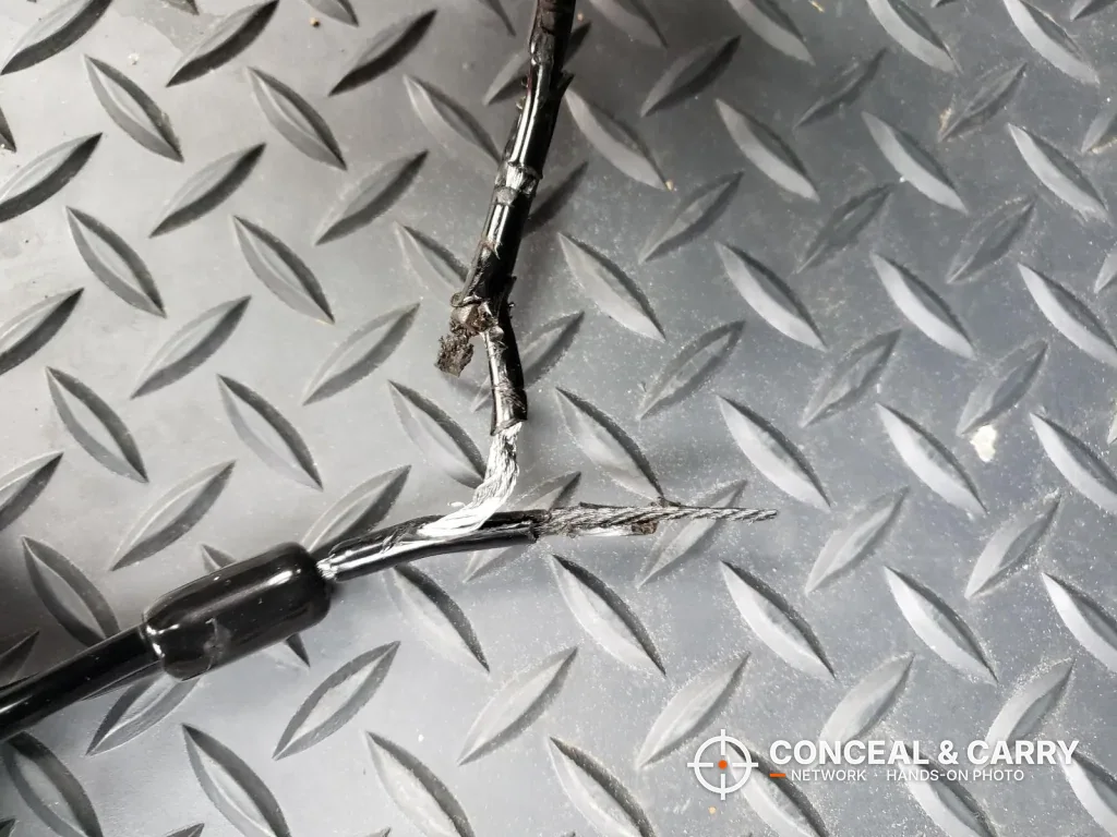 Hornady Lockbox cable cut through with frayed steel strands on a floor mat
