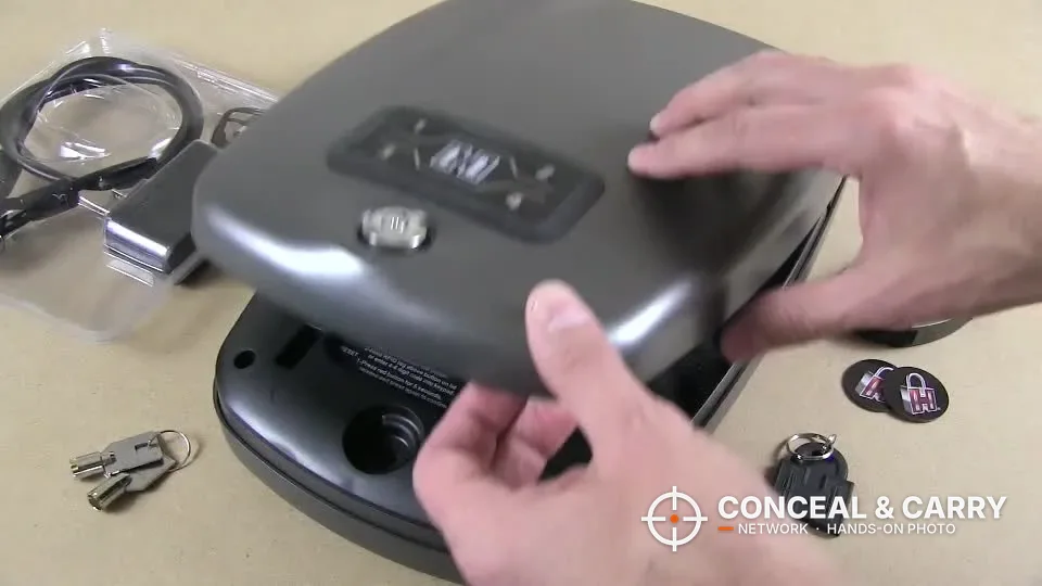 Lifting the lid of the Hornady RAPiD Safe RFID with keys, stickers and a fob on the table