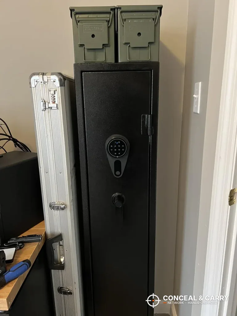 KAER long gun safe in a corner with two ammo cans on top and a rifle case beside it