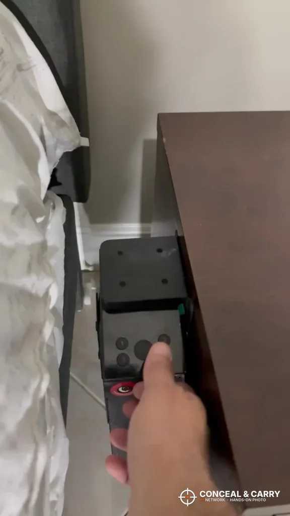Hand reaching down to the top of the KornerBatl safe beside a bed