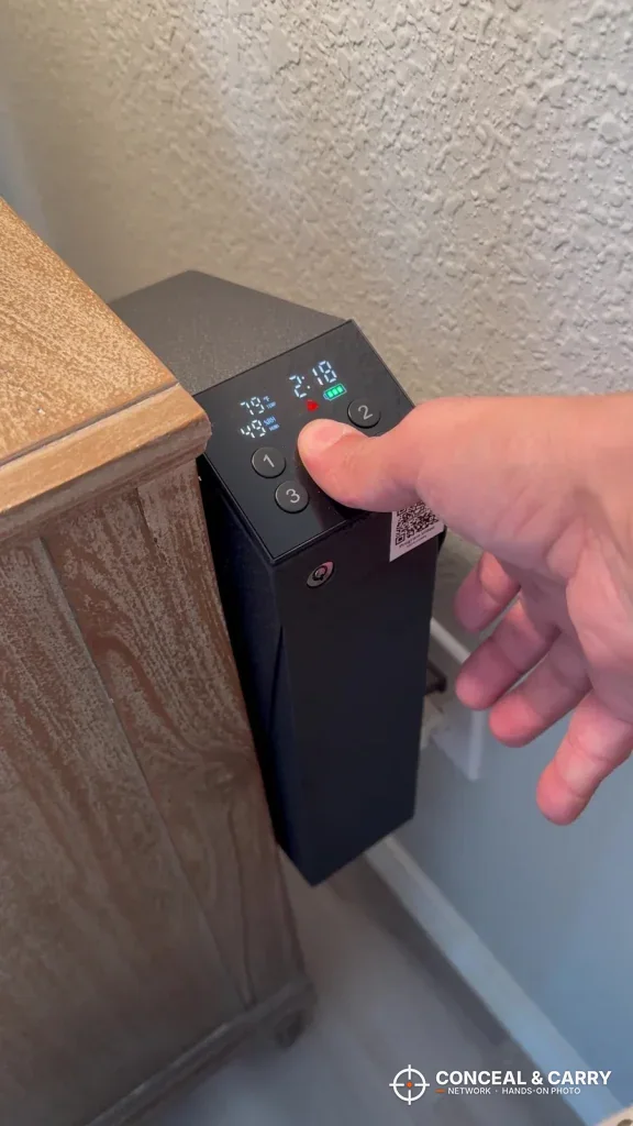 Hand reaching for the KornerBatl safe mounted on a wooden nightstand