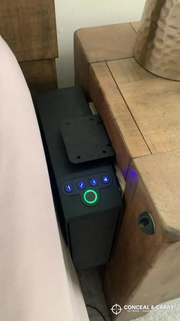 Langger slider safe beside a nightstand with the keypad lit blue and the reader ringed green