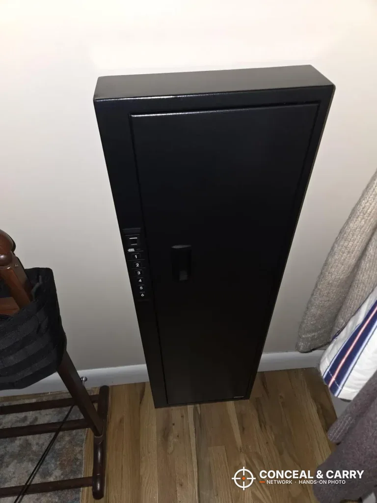 Langger compact long gun safe mounted on a wall above the floor beside a chair