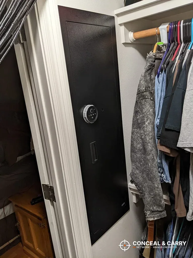 Black Langger in-wall safe set into a closet wall beside hanging clothes