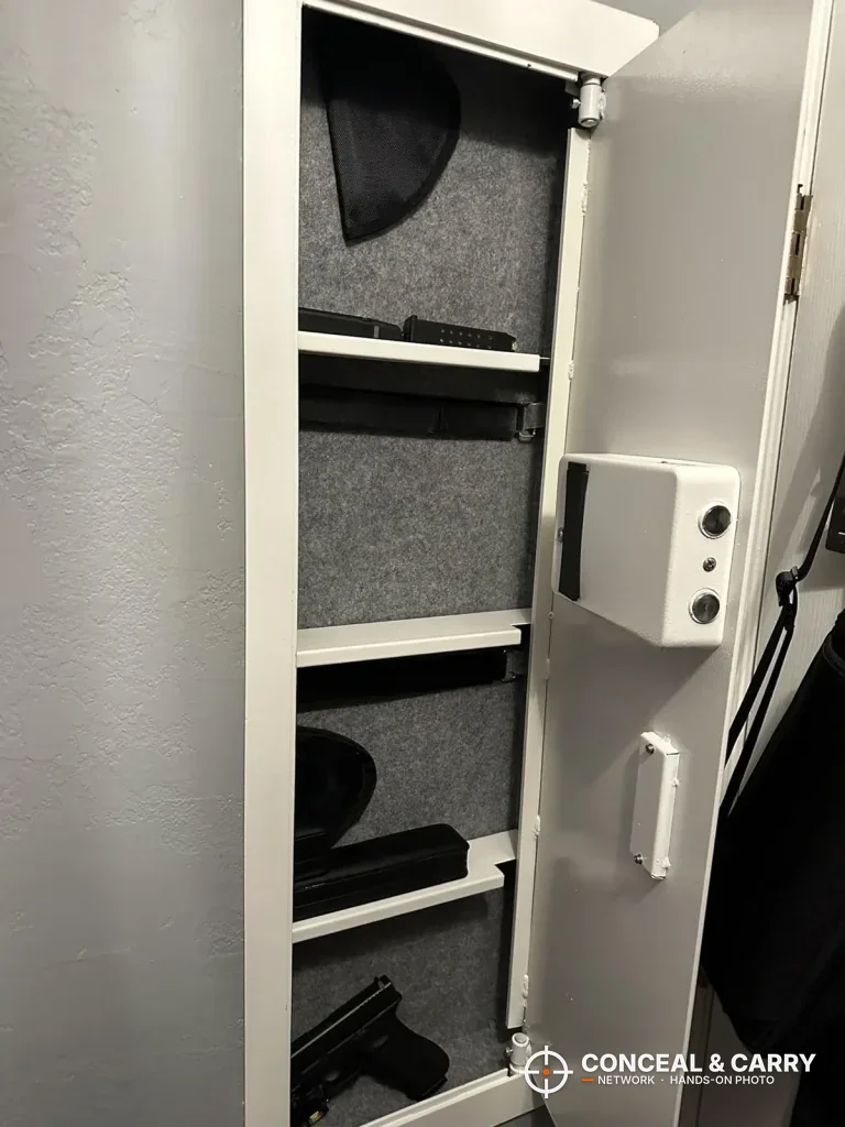 White Langger in-wall safe open with gray-lined shelves holding handguns