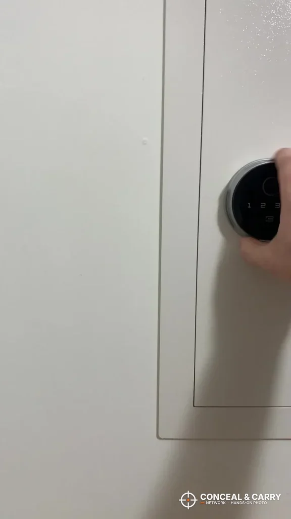 Round fingerprint and keypad control on the door of a white Langger in-wall safe