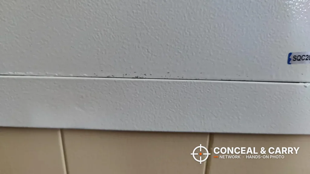 Seam between the door and frame along the bottom edge of a white Langger in-wall safe