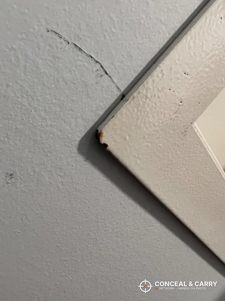 Corner of the Langger in-wall safe trim flange with a hairline crack in the drywall