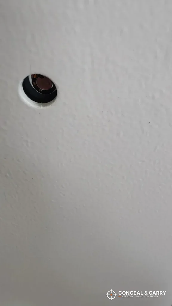 Close-up of a small round opening in the textured white finish of a Langger in-wall safe