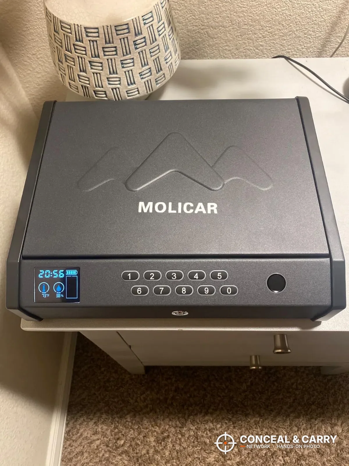 MOLICAR biometric bedside safe closed on a white nightstand with the screen lit