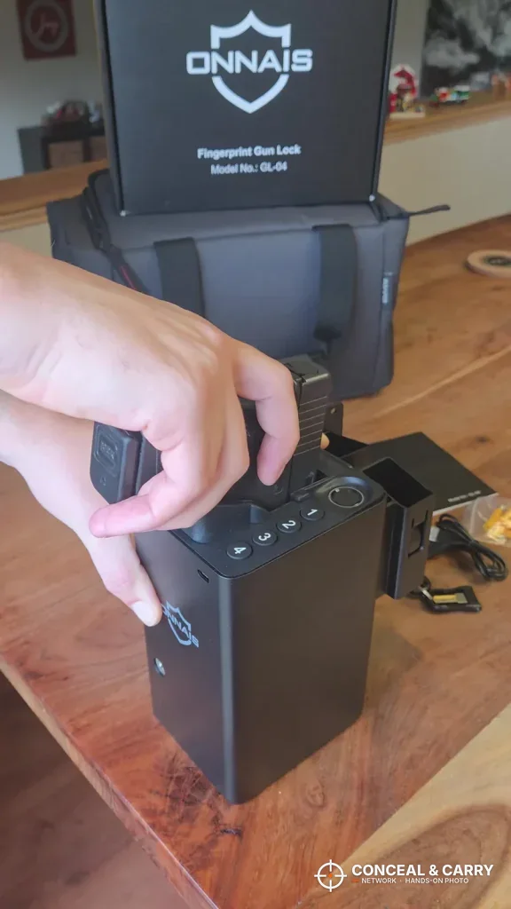 Hand on the grip of a pistol in the ONNAIS open-design safe beside its box