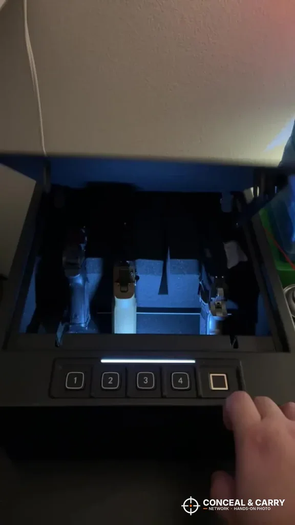 Finger on the RPNB 4-pistol safe fingerprint pad in a dark room with the light bar lit
