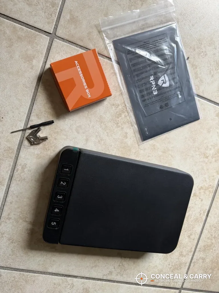 RPNB car gun safe closed on a tile floor beside the manual and small parts
