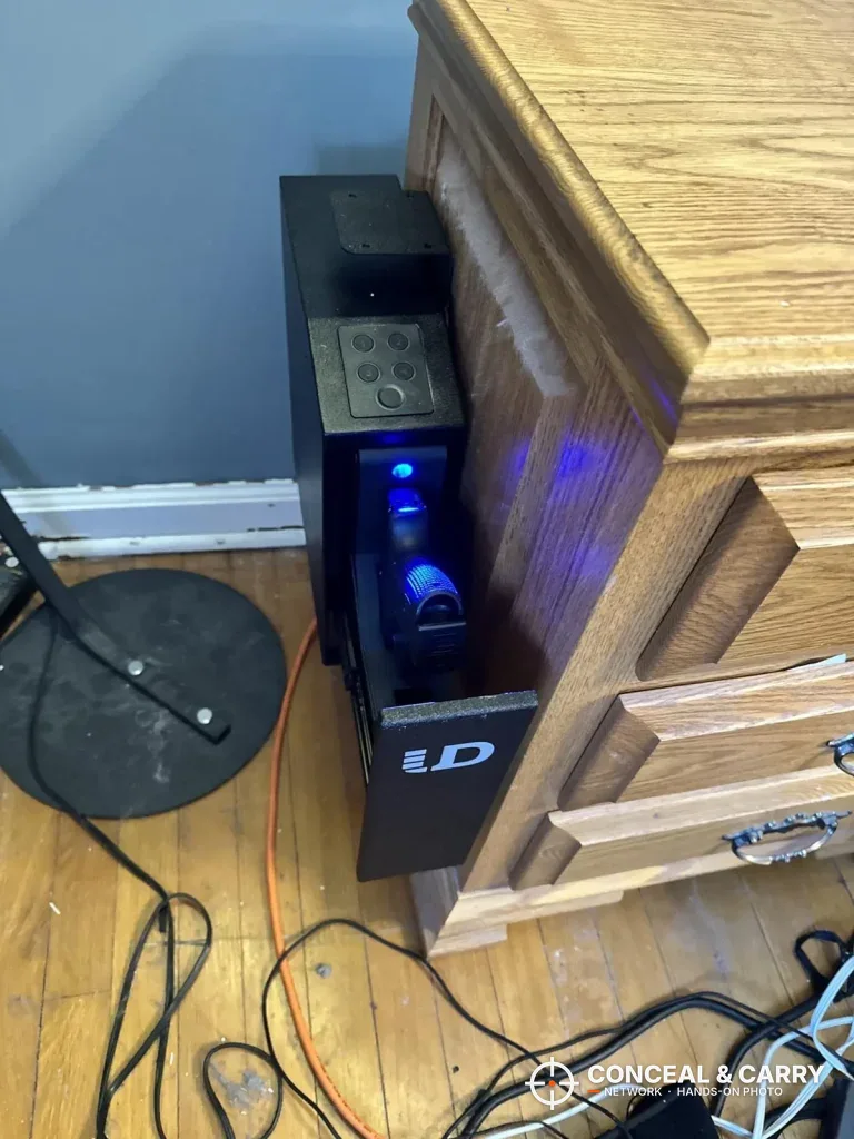 Urban Deco pistol safe beside a nightstand with the door open and lit inside