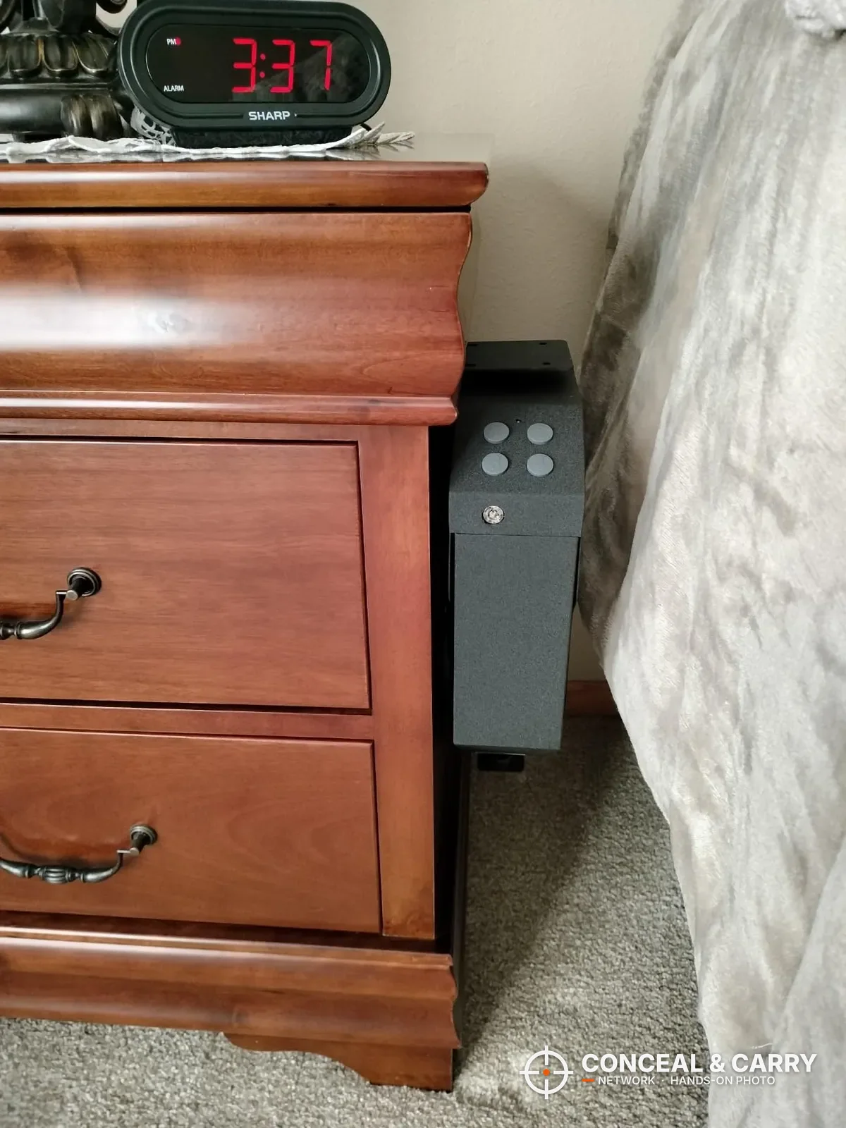 VERPROOF keypad gun safe standing beside a wooden nightstand next to the bed