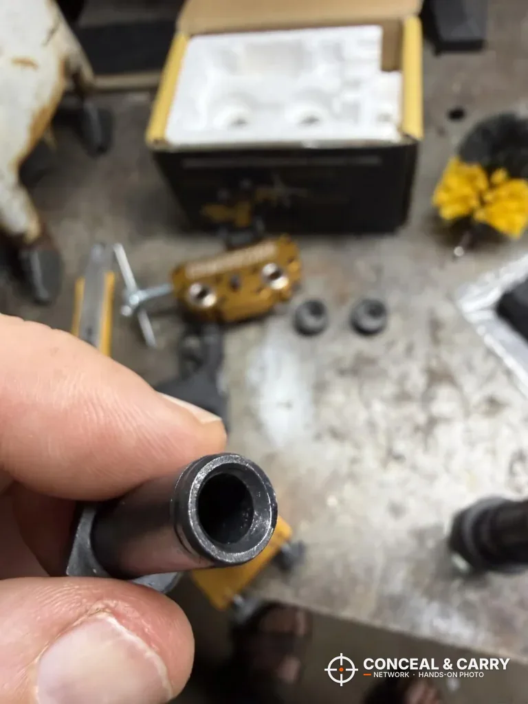 Small black part from the Wheeler sight tool kit held over the bench, open box behind